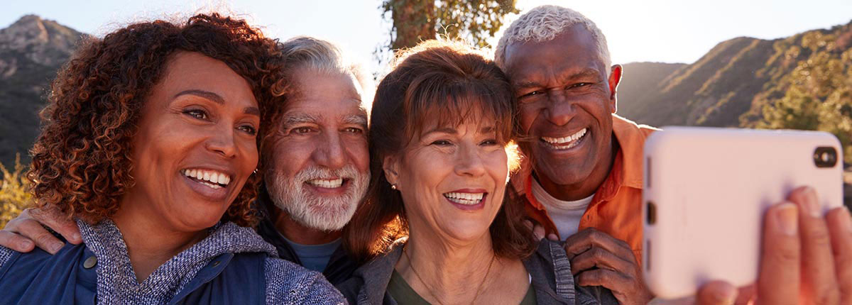 4 friends taking a selfie in an outdoor setting smiling with their fixed dentures on implants