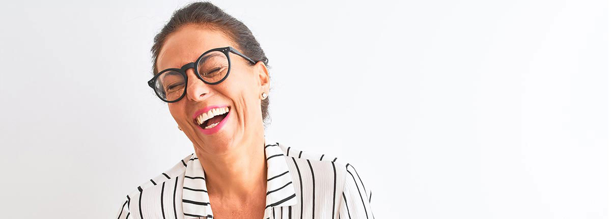 An image of a woman wearing a black and white striped shirrt having a good laugh while squinting through her round dark rimmed glasses