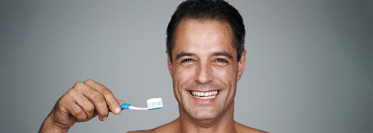 A man sporting a big smile holding a toothbrush in front of a grey background