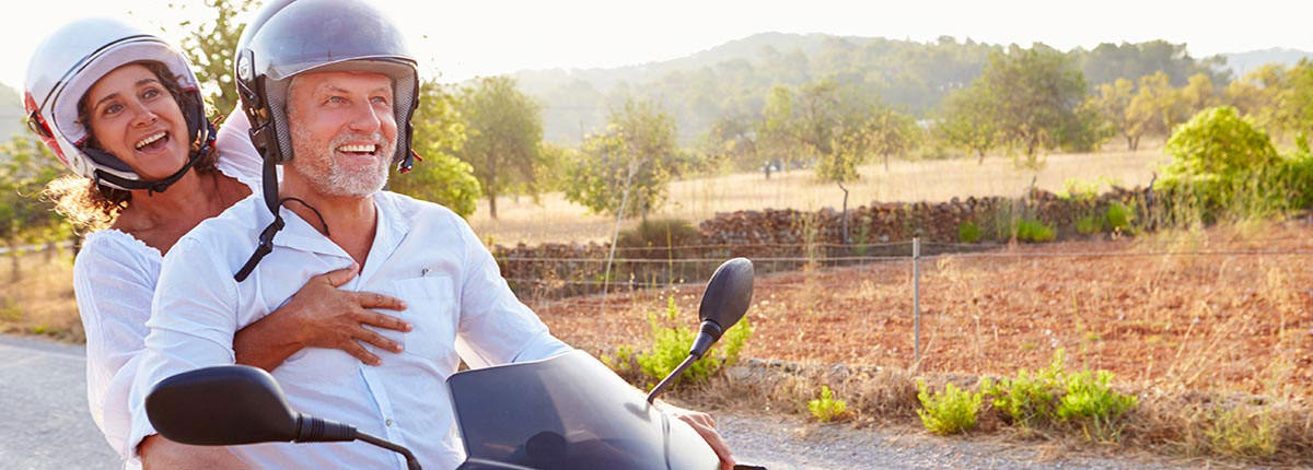 A mature couple in white shirts riding the countryside on a moped