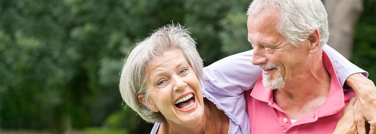 An image of a couple laughing and being silly against a wooded background