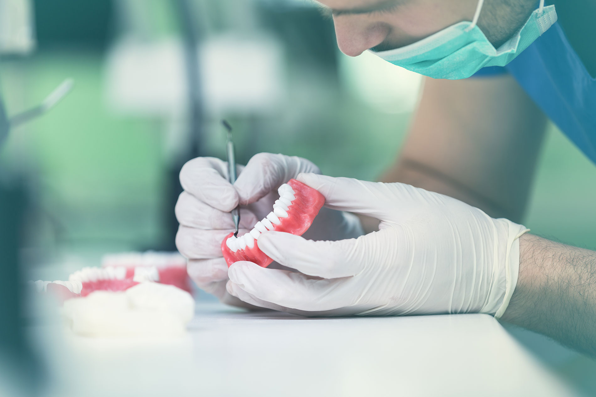The hands of a denture technician making adjustments to a partial denture with dental pick